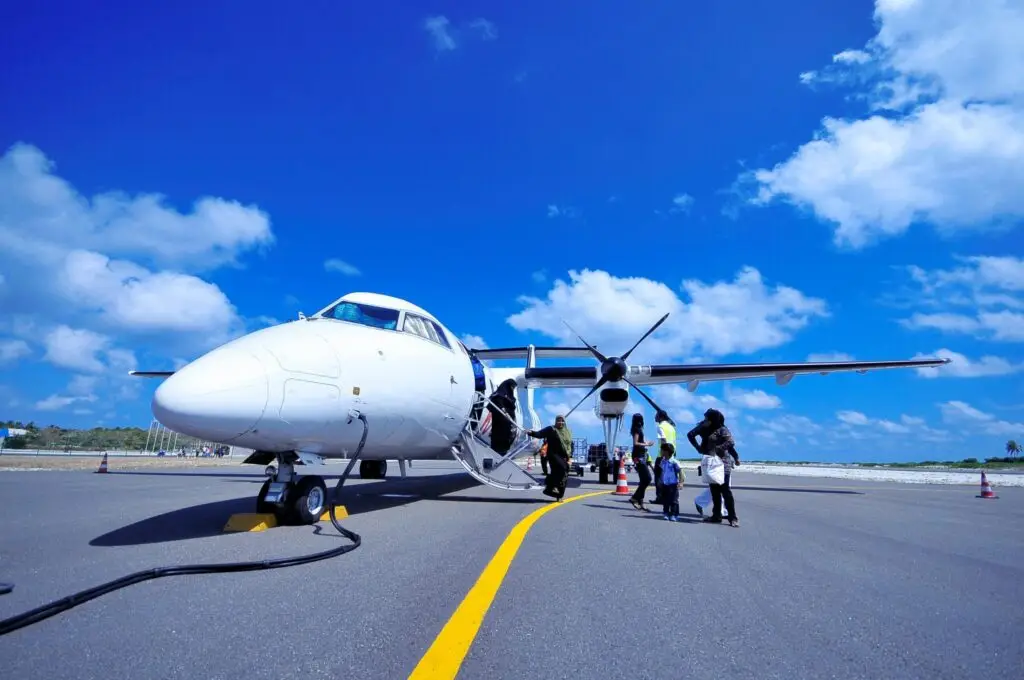 A group of people board a propeller airplane on a sunny day in Fuvahmulah, Maldives.
