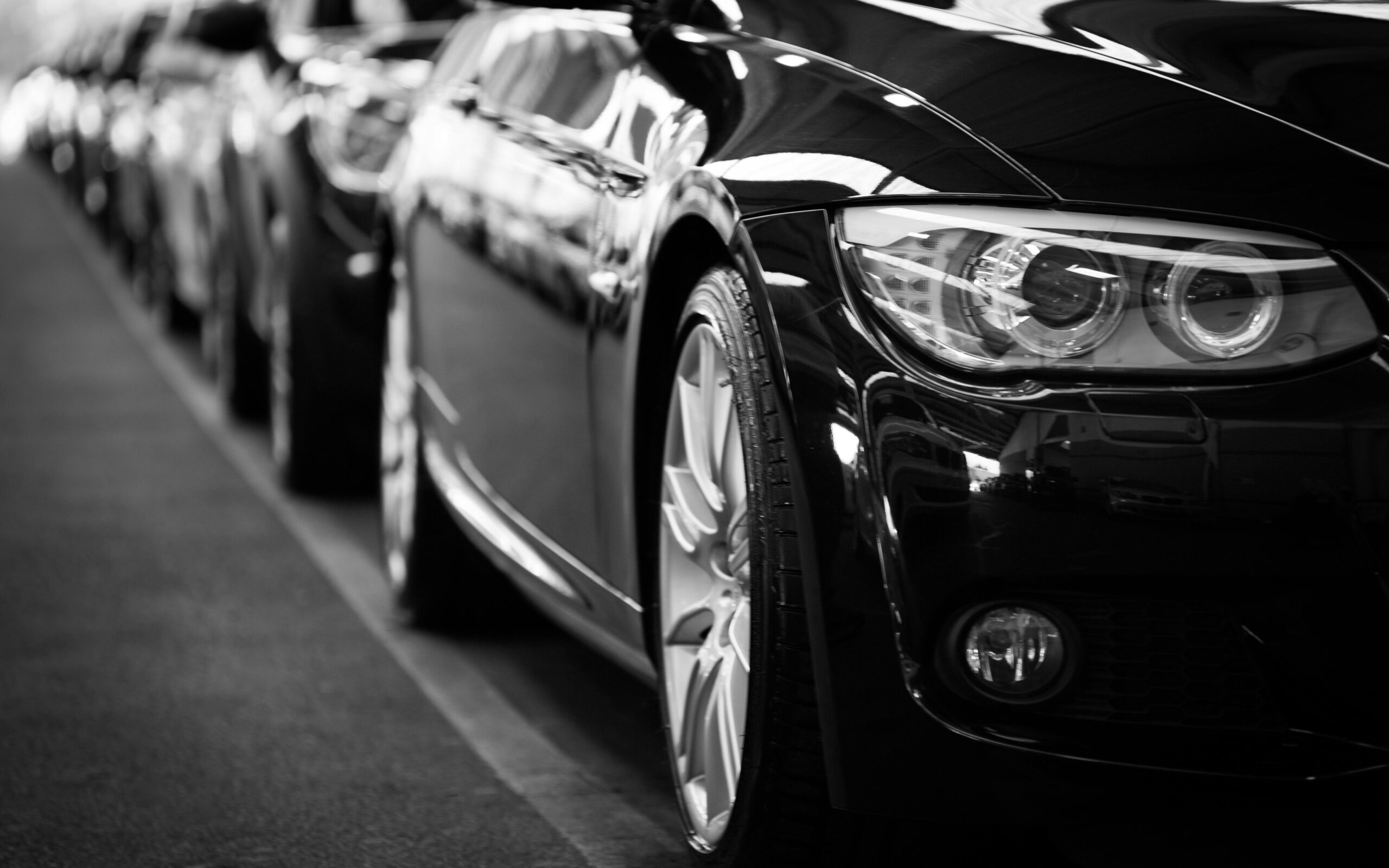 Close up black and white image of a luxury car line up focusing on vehicle headlights