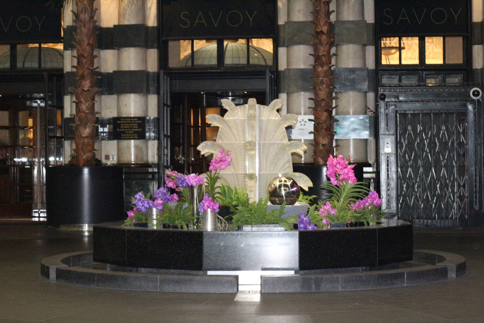 The Savoy Hotel entrance fountain with flowers and illuminated Savoy signage in London