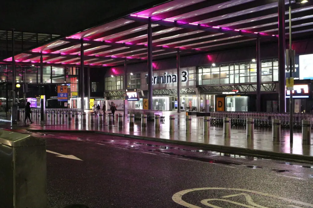 Exterior view of London Heathrow Terminal 3 at night with pink canopy lights and wet pavement, representing premium airport transfer chauffeur service in London.