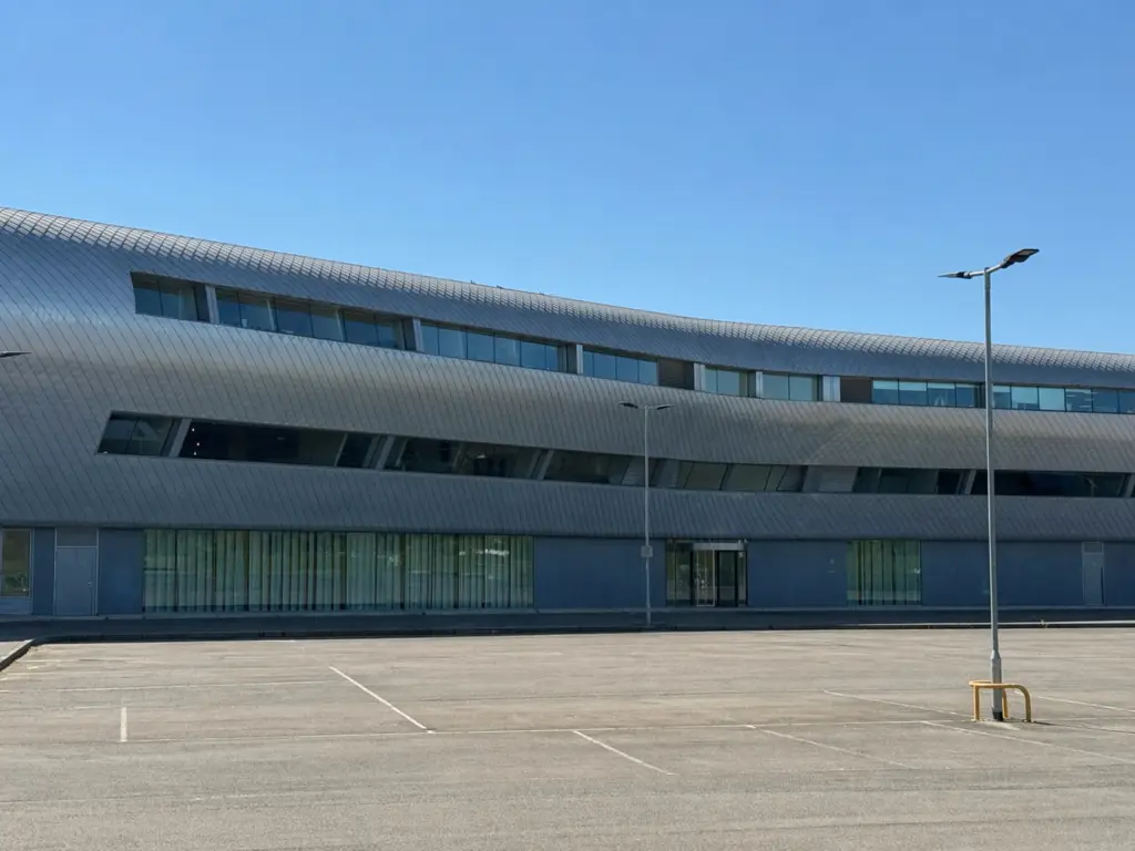 Modern Farnborough Airport terminal building with parking area under a clear blue sky.