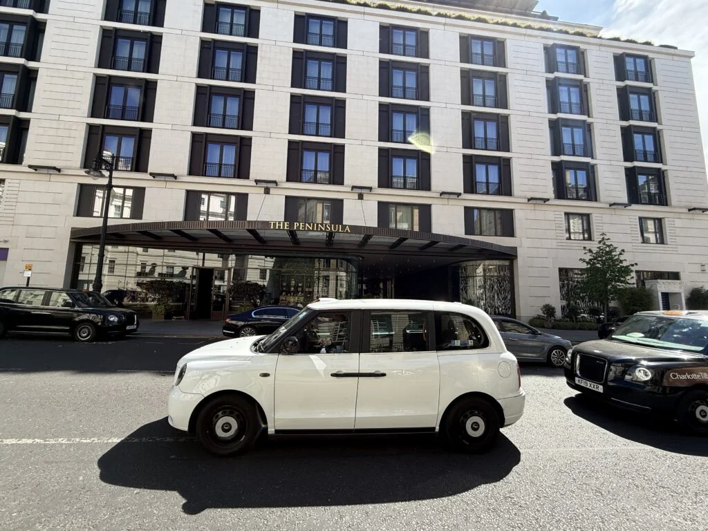 The Peninsula London hotel entrance and pale stone façade, with a white London taxi in the foreground.